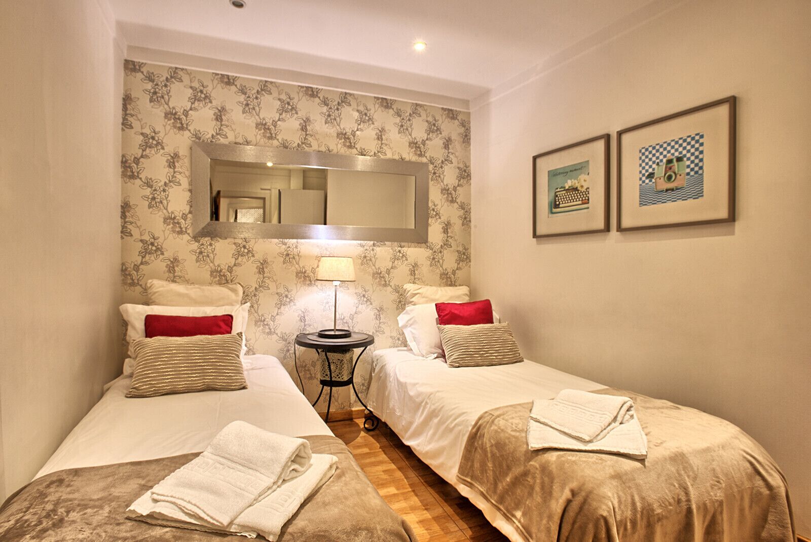 Una habitación de hotel con dos camas individuales, una mesita, una lámpara y un espejo en la pared.