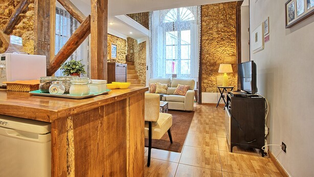 A cozy living area with a wooden bar, a sofa, a television, and a stone wall. - Tv1 - Alfama Retreat | AC | 3 Bedrooms sleeps 10 walk everywhere (Lisbon)