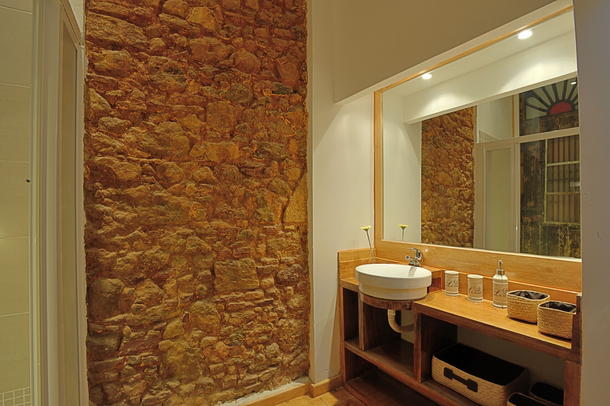 A bathroom with a stone wall, a wooden vanity, a large mirror, and a white sink.