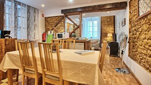A dining area with wooden chairs and a table, a kitchen area with appliances, and a stone wall. - Tv1 - Alfama Retreat | AC | 3 Bedrooms sleeps 10 walk everywhere (Lisbon)