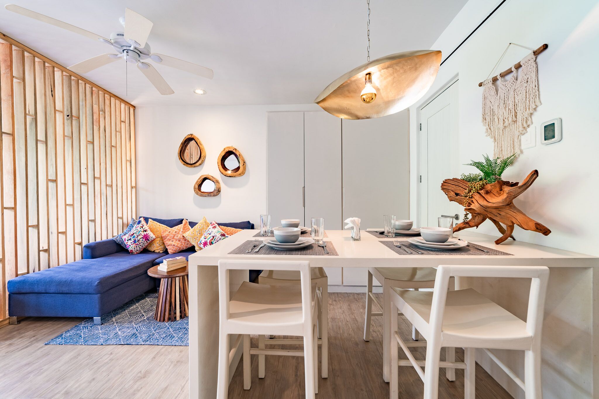 Un soggiorno moderno con un divano, un tavolo da pranzo e sedie. Si nota una ventola a soffitto, luci a parete e decorazioni murali.