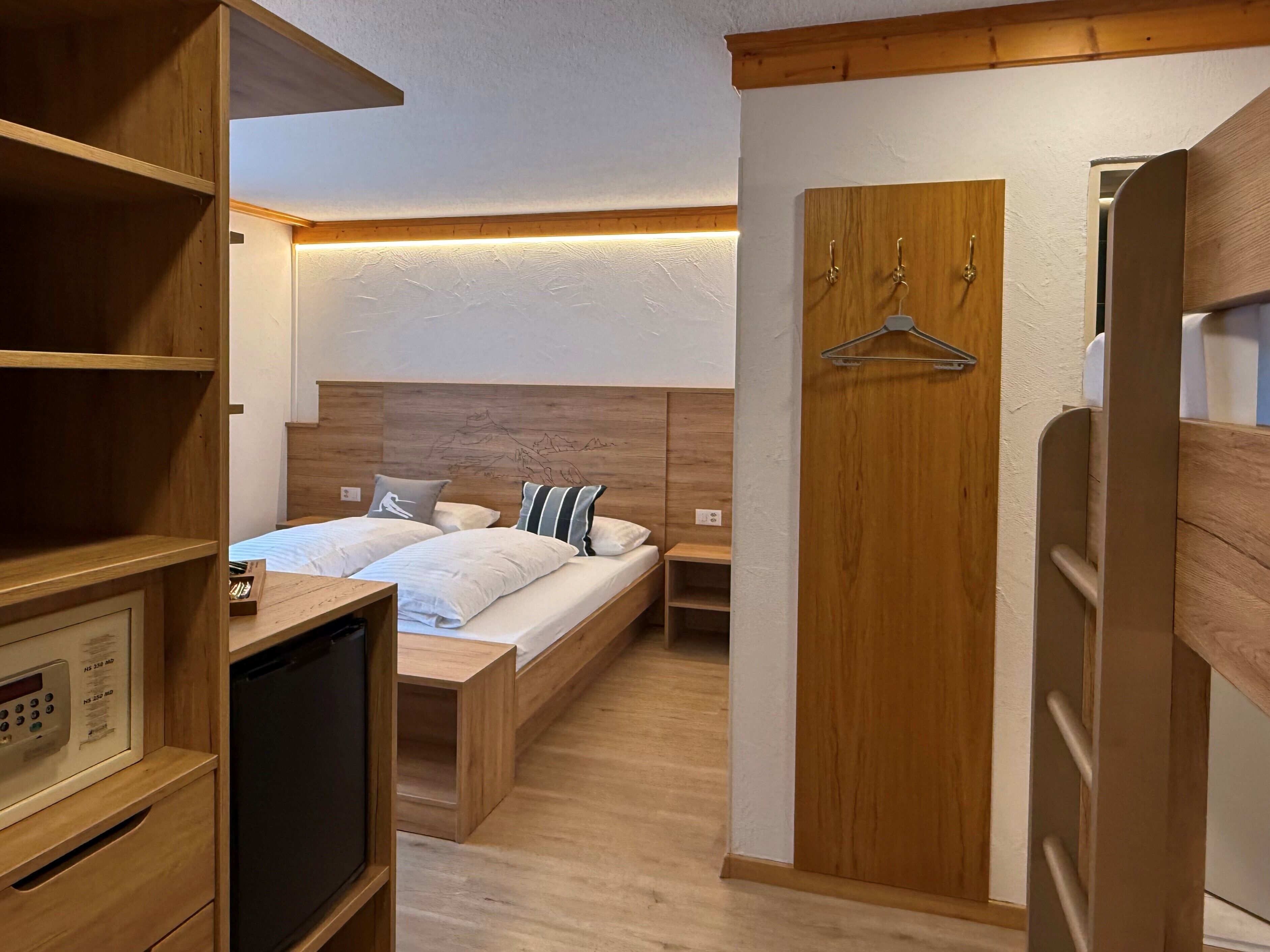 Une chambre avec deux lits, une tête de lit en bois, des tables de chevet, une télévision et une armoire avec un portant.