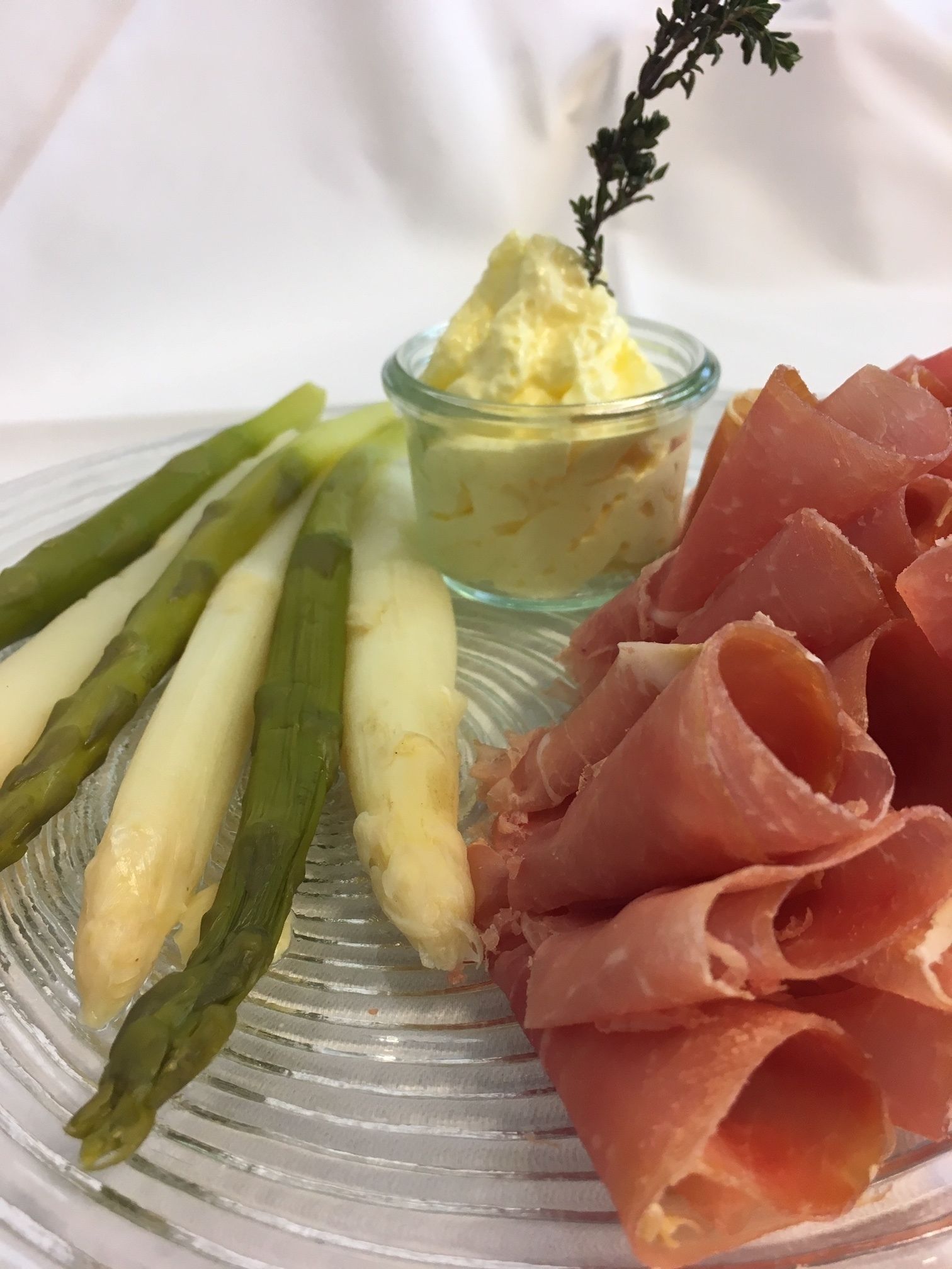 A plate with asparagus, a small bowl of butter, and slices of prosciutto.