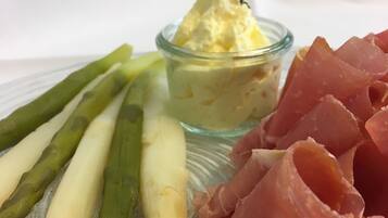A plate with asparagus, a small bowl of butter, and slices of prosciutto.