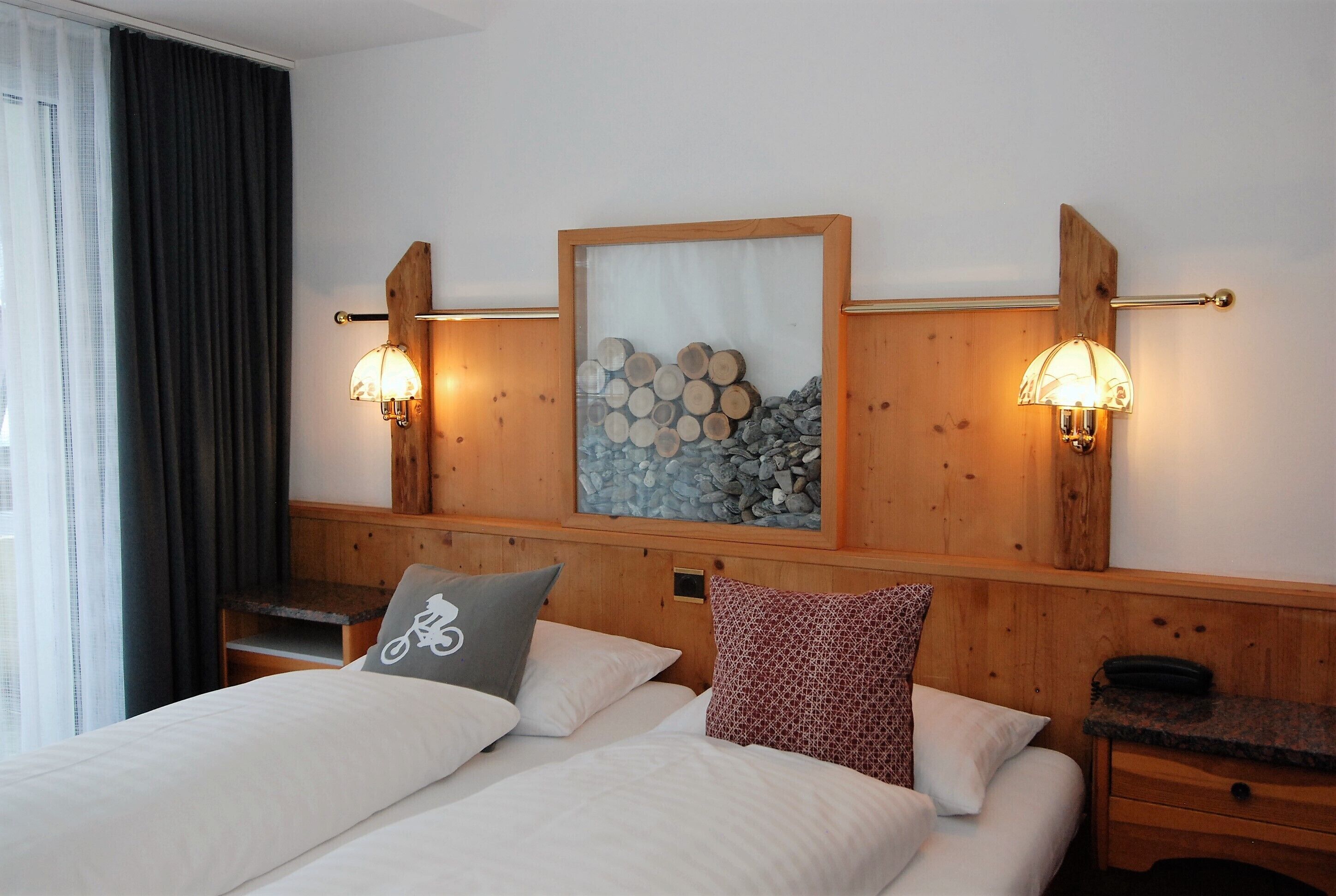 Habitación de hotel con dos camas, cabecero de madera, lámpara de pared y un cuadro con motivos de troncos.