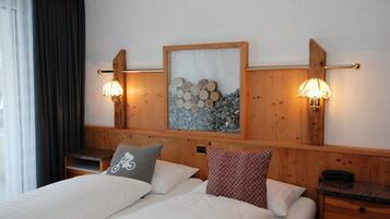 Habitación de hotel con dos camas, cabecero de madera, lámpara de pared y un cuadro con motivos de troncos.