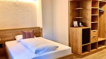 A neatly made bed with a wooden headboard, a wooden wardrobe with shelves, and a wall-mounted light fixture.