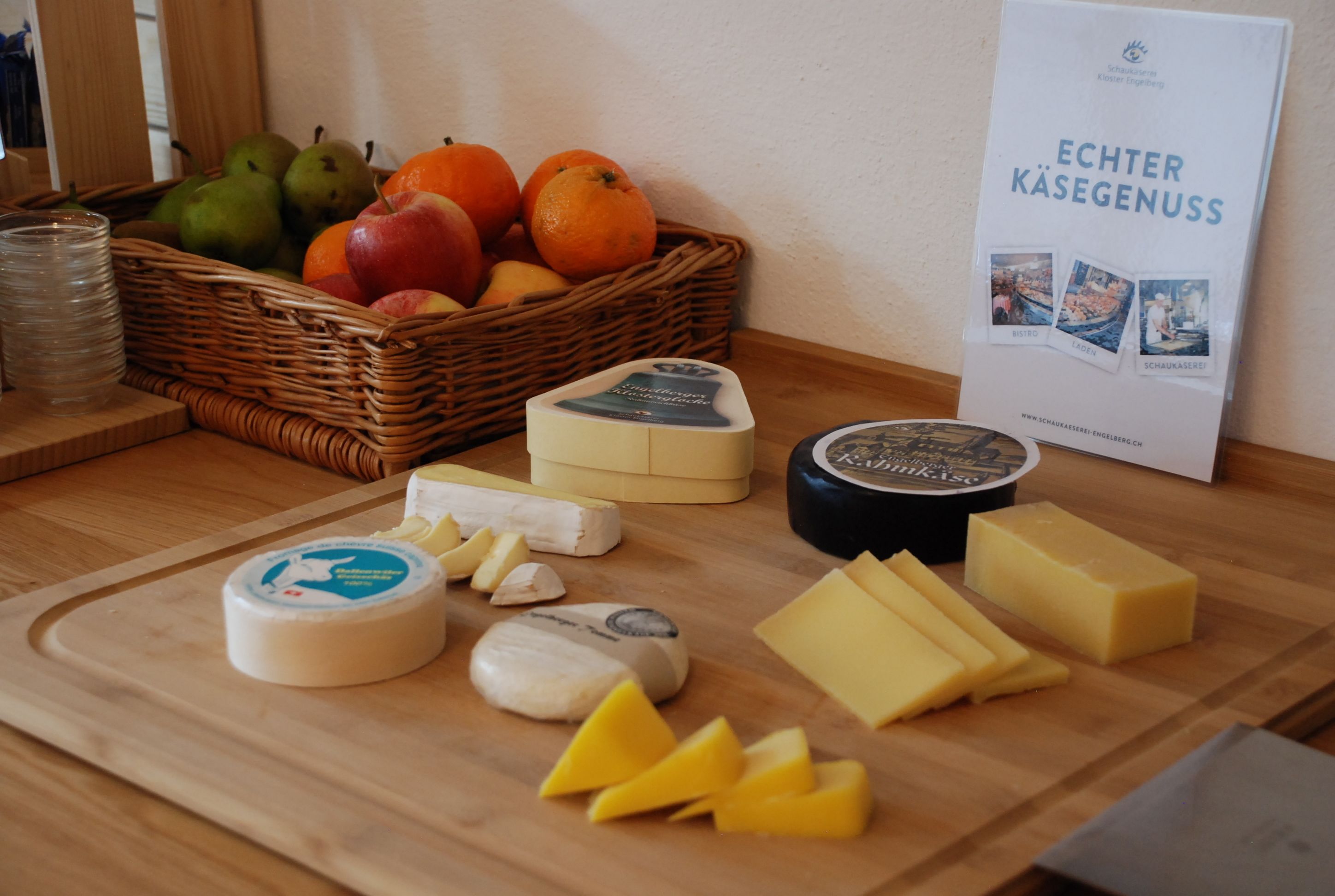 Une planche à découper en bois, sur laquelle sont disposés différents fromages, et un panier de fruits.
