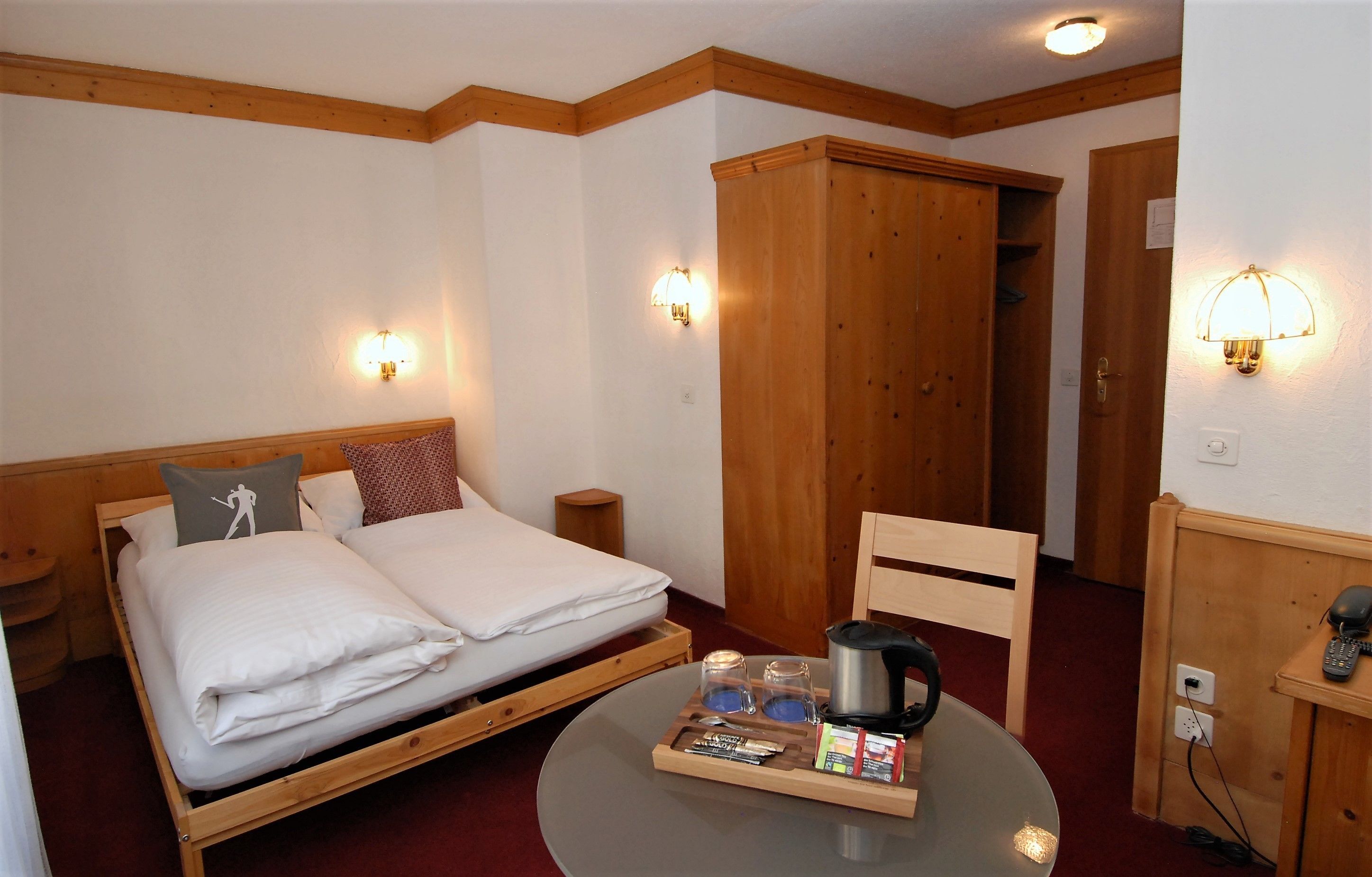 Een kamer met een houten bed, twee nachtkastjes, een klein rond tafeltje met een dienblad met ontbijtartikelen, een houten kledingkast en twee wandlampen.