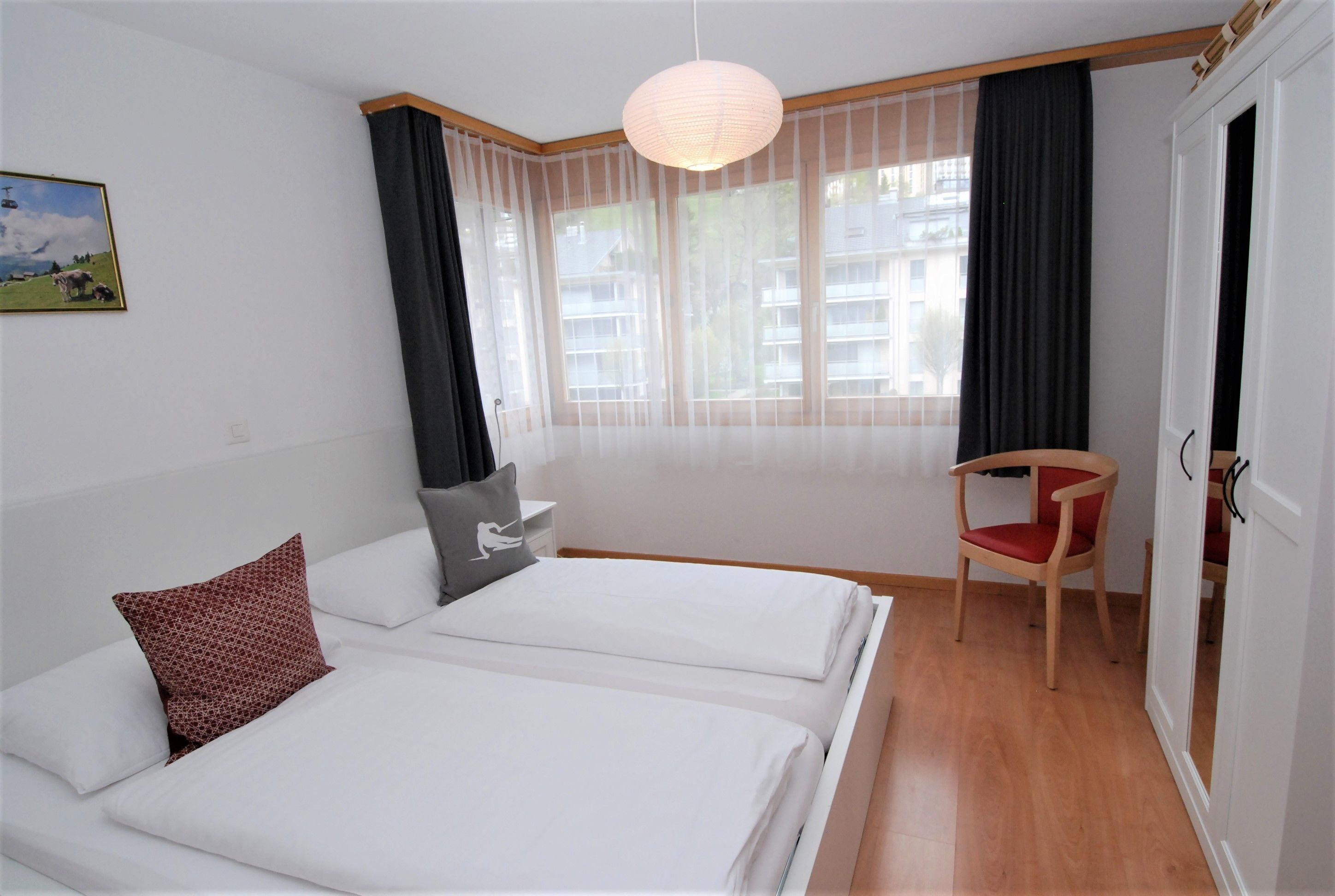 A hotel room with two beds, a chair, a desk, and a large window with curtains.