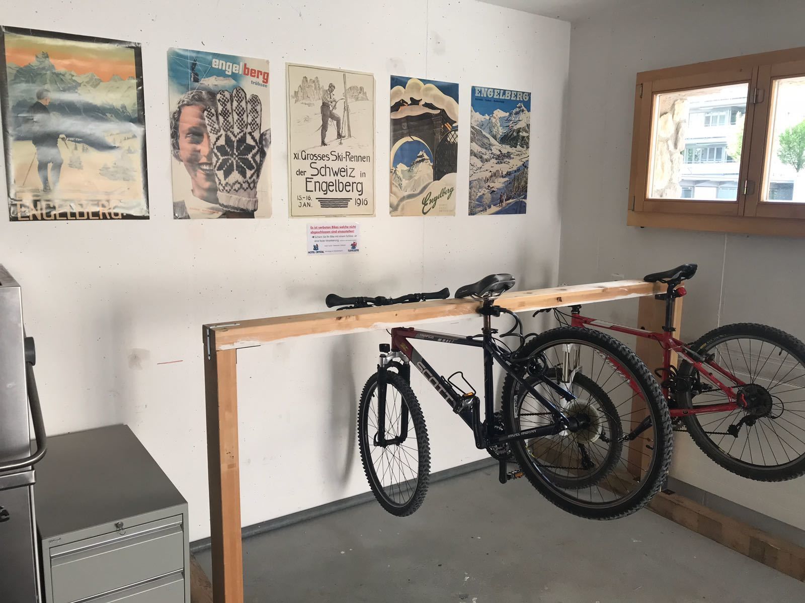 Een kamer met een fietsenrek, daarin twee fietsen, een metalen archiefkast en vier posters aan de muur.