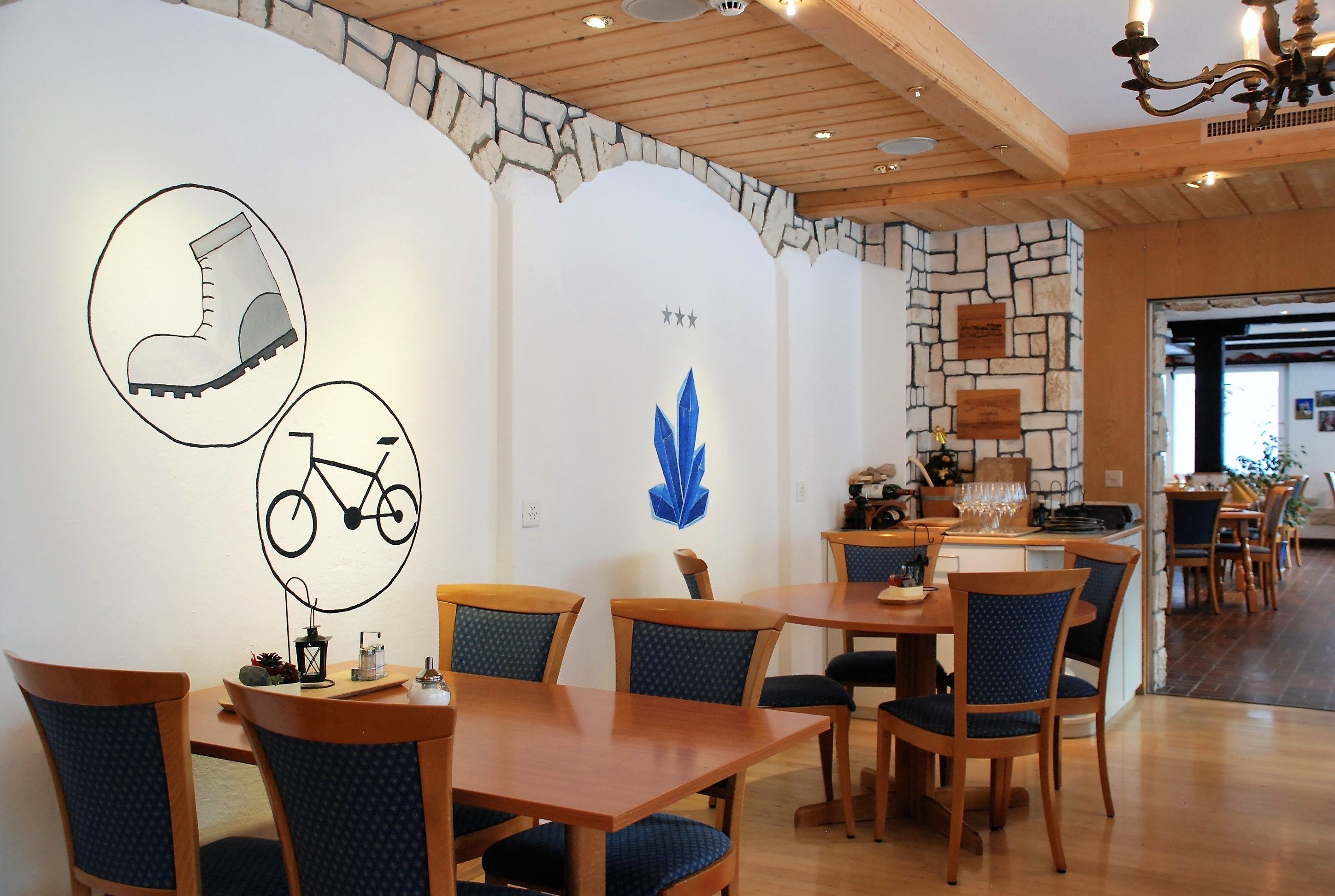 A dining area with wooden tables and chairs, stone walls, and a chandelier.
