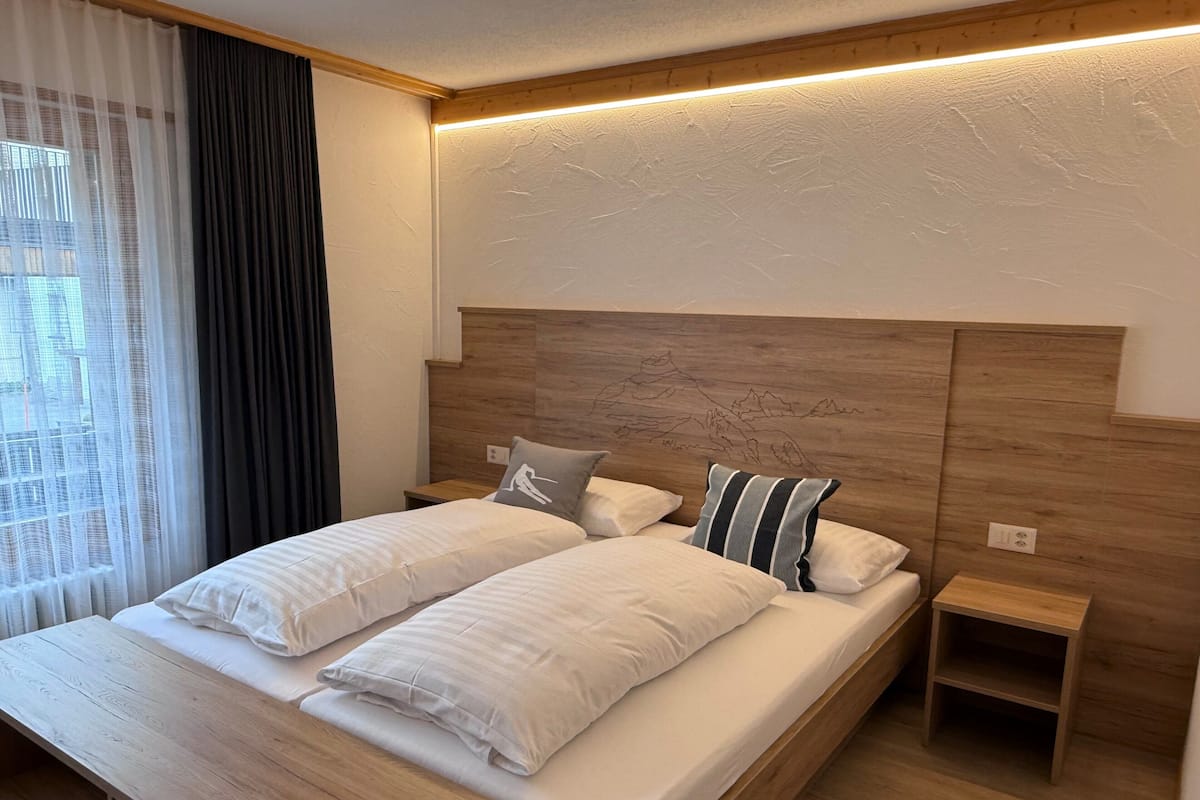 Une chambre d’hôtel moderne avec un lit en bois, deux tables de chevet et une tête de lit ornée d’un motif de montagne.