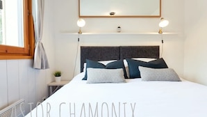 A neatly arranged bedroom with a large bed, a headboard, bedside lamps, and a mirror above the bed. - Stunning panoramic view, Cham centre, Pkg & WIFI (Chamonix-Mont-Blanc)