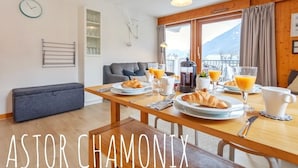 A dining area with a wooden table set for breakfast, including croissants, orange juice, and coffee. - Stunning panoramic view, Cham centre, Pkg & WIFI (Chamonix-Mont-Blanc)