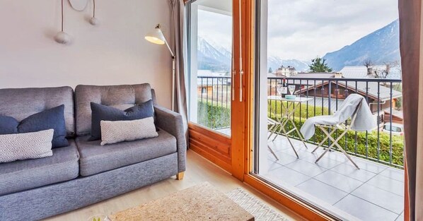 A modern living room with a grey sofa, a small table, and a balcony with outdoor seating. - Stunning panoramic view, Cham centre, Pkg & WIFI (Chamonix-Mont-Blanc)