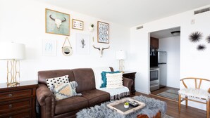 Un salon avec un canapé en cuir marron, une table basse en bois et un coin repas comprenant une chaise en bois et une chaise blanche.