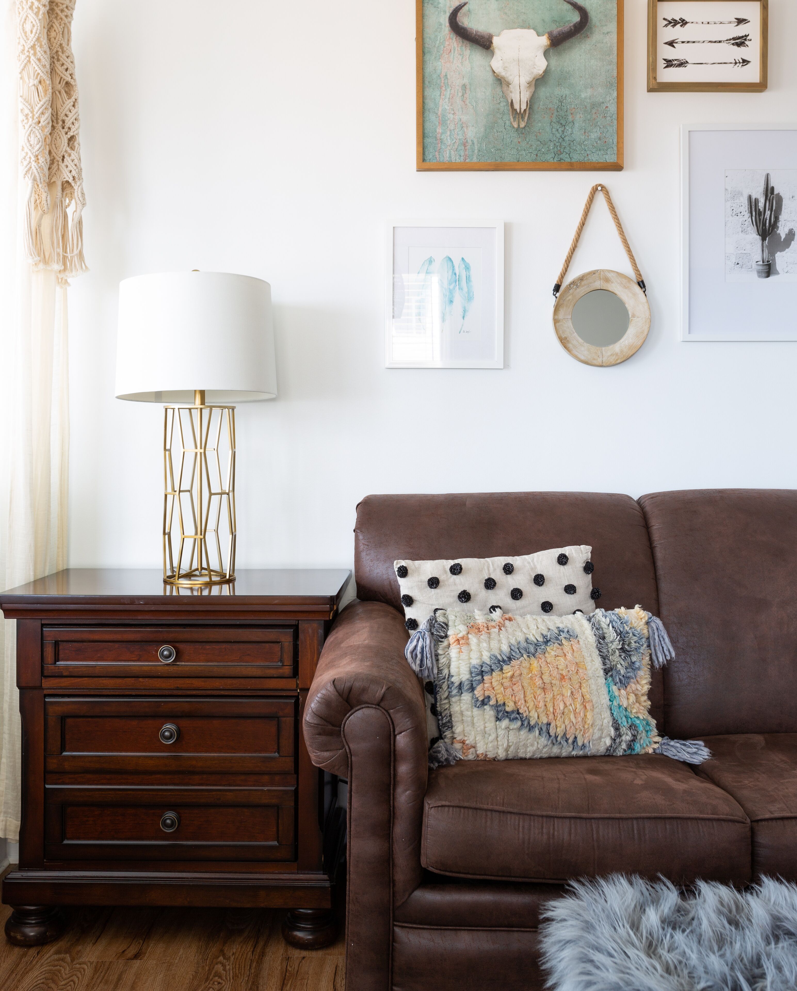 Ein Wohnzimmer mit einem braunen Ledersofa, einem Holzbeistelltisch mit einer Lampe und verschiedenen Wandbildern, darunter ein Schädel und Pfeile.