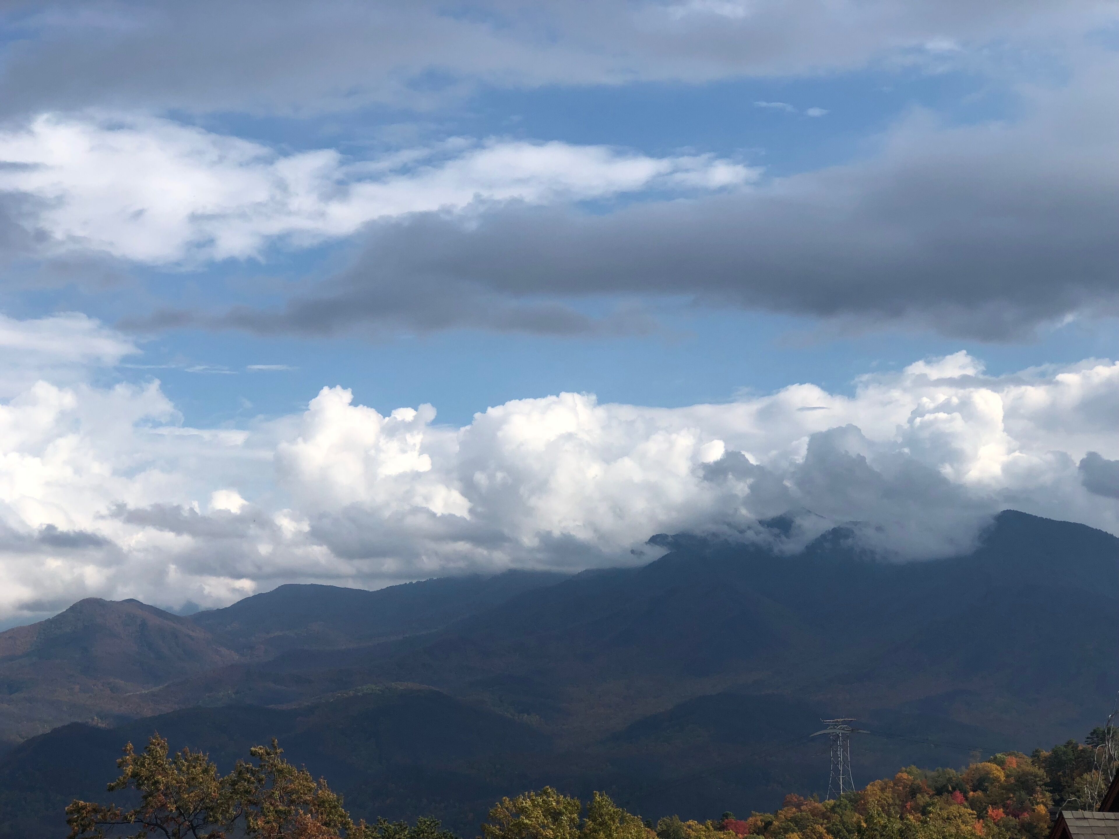 Paisatge de muntanya amb núvols, arbres i una línia elèctrica.