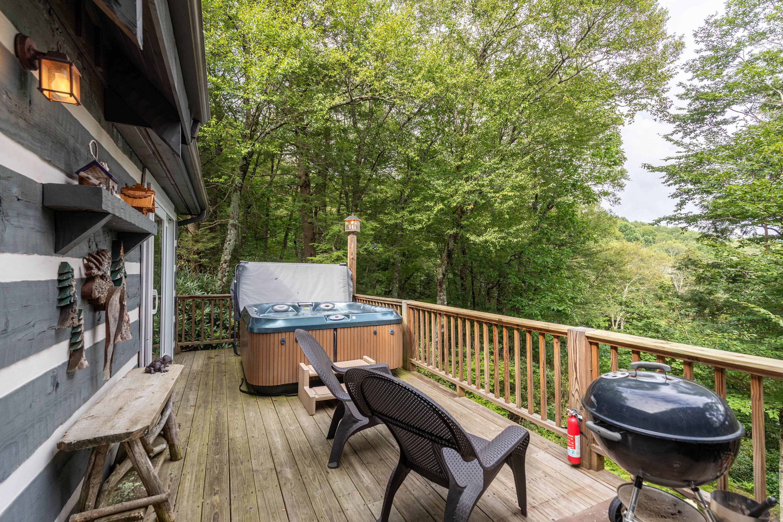 Een houten terras met een jacuzzi, barbecue en buitenmeubels.