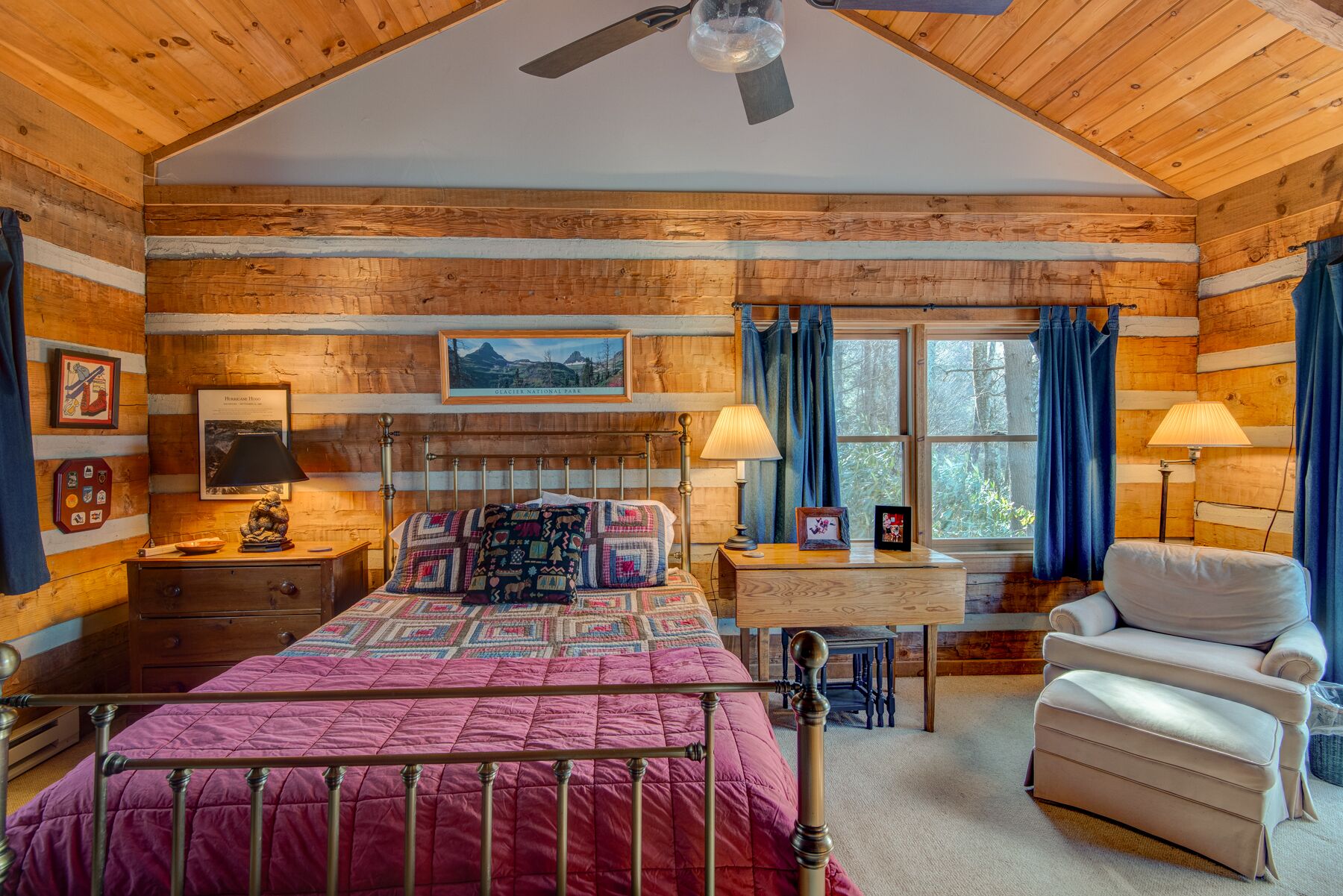 A cozy log cabin bedroom with a bed, two bedside tables, a chair, and a window with curtains.