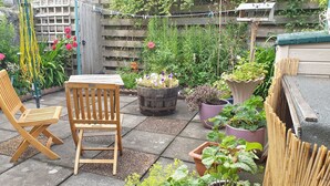 Een houten stoel en tafel in een tuin, met verschillende planten in potten en een houten hek.