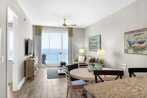A modern living room with a dining area, large windows, and a view of the sea.