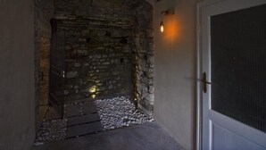 A stone-walled entrance with a metal gate, a concrete path, and a door with a screen. - Goldenlake Apartment (Perledo)