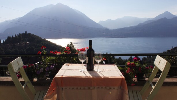 A table with a bottle and glasses, overlooking a lake and mountains. - Goldenlake Apartment (Perledo)