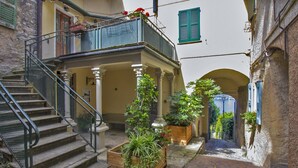 A narrow stone-paved alley with a wooden staircase leading to a balcony. There are potted plants and a small wooden bench on the steps. - Goldenlake Apartment (Perledo)