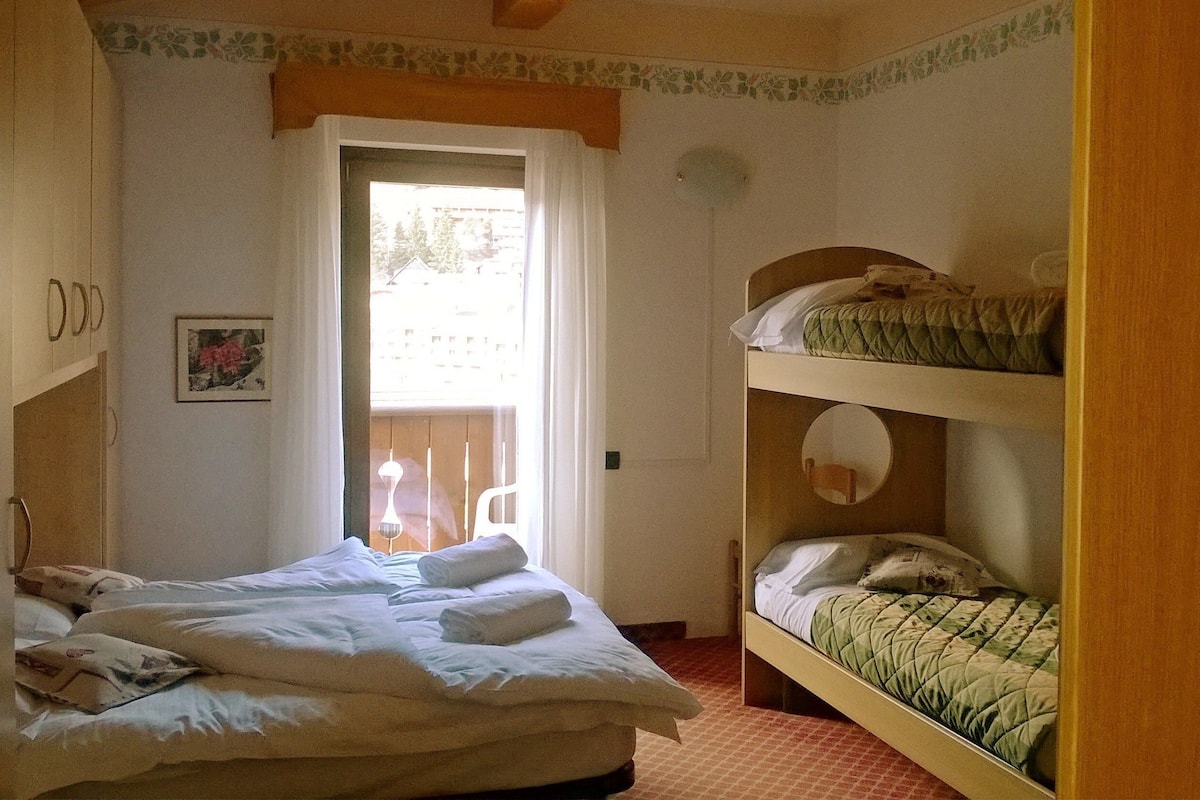 A room with a single bed, a bunk bed, a door leading to a balcony, and a small table with a chair.