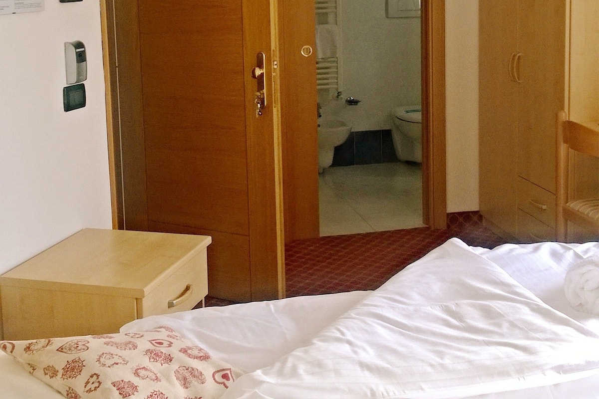 A hotel room with a bed, wooden wardrobe, and a bathroom visible through an open door.