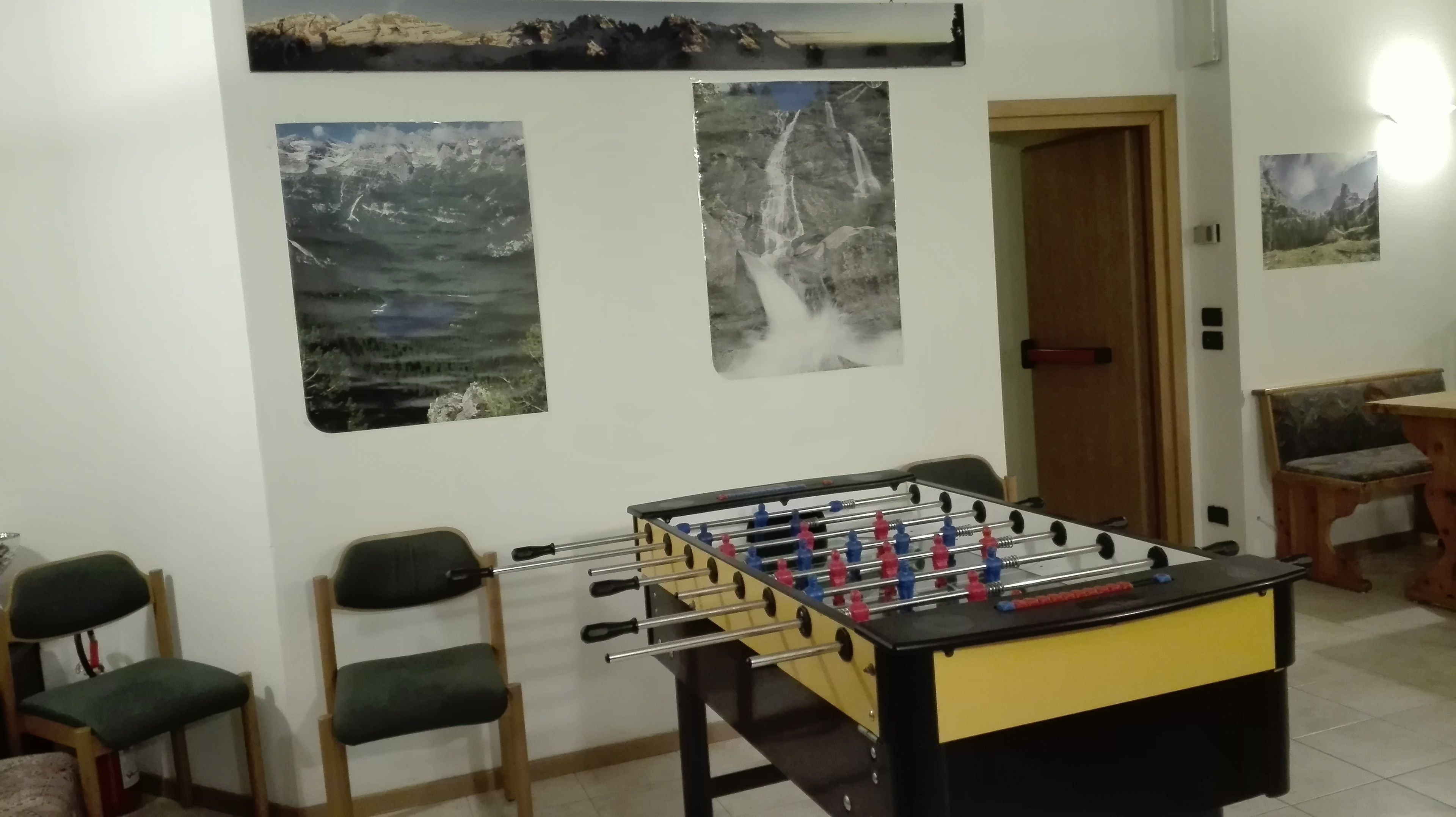 A room with a foosball table, two chairs, and three framed pictures on the wall.