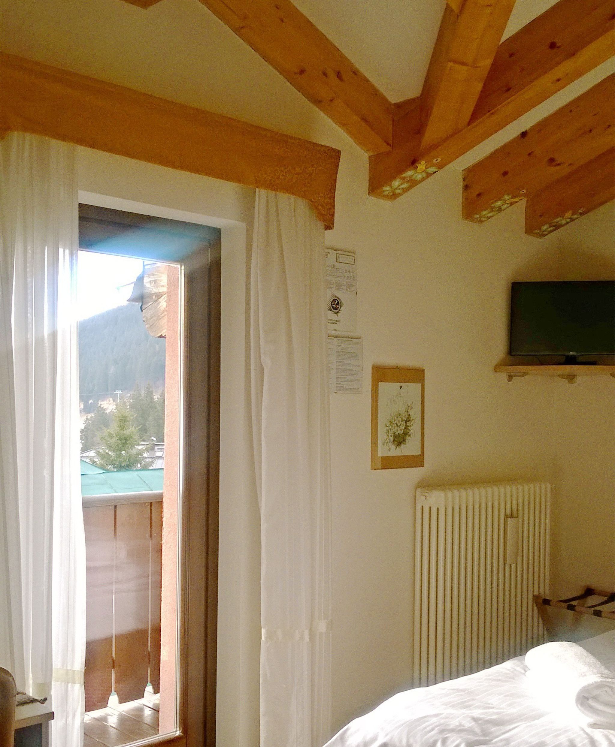 Un dormitorio con techo de madera, una cama con ropa blanca, un radiador y un televisor en una estantería.