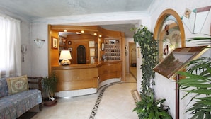 A lobby with a reception desk, a sofa, and a wall-mounted mirror. - Villa Emma (Tre Ville)