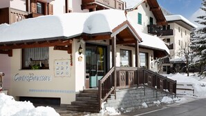 A snow-covered building with a wooden staircase leading to a door marked "CentroBenessere." - Villa Emma (Tre Ville)