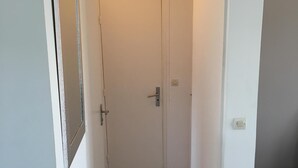 A narrow hallway with a wooden floor, a white door with a silver handle, and a wall-mounted light fixture. - T3 ROUEN docks side with free parking - 4 BEDS (ROUEN)