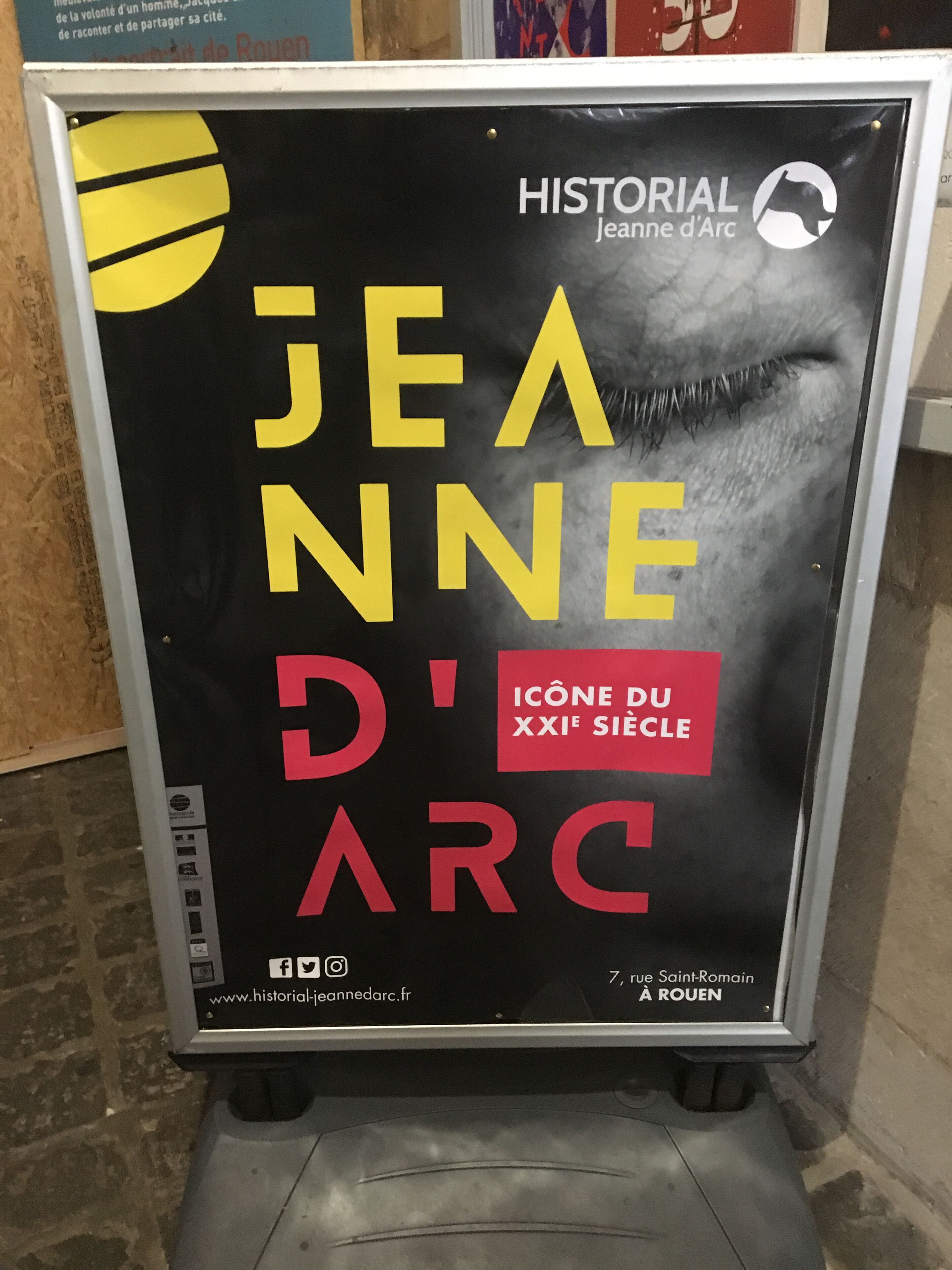A poster with text and a graphic, likely for an event or exhibition, displayed on a stand.