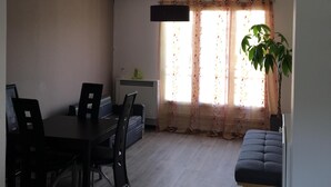 A dining area with a table and chairs, a hanging light fixture, a window with curtains, and a potted plant. - T3 ROUEN docks side with free parking - 4 BEDS (ROUEN)