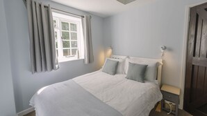 Ein Schlafzimmer mit Bett, Vorhängen, einem Fenster, einem Nachttisch und einer Wandleuchte.