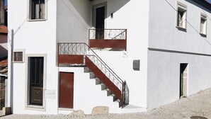 A two-story building with a white exterior, a wooden door, and a staircase with metal railings.