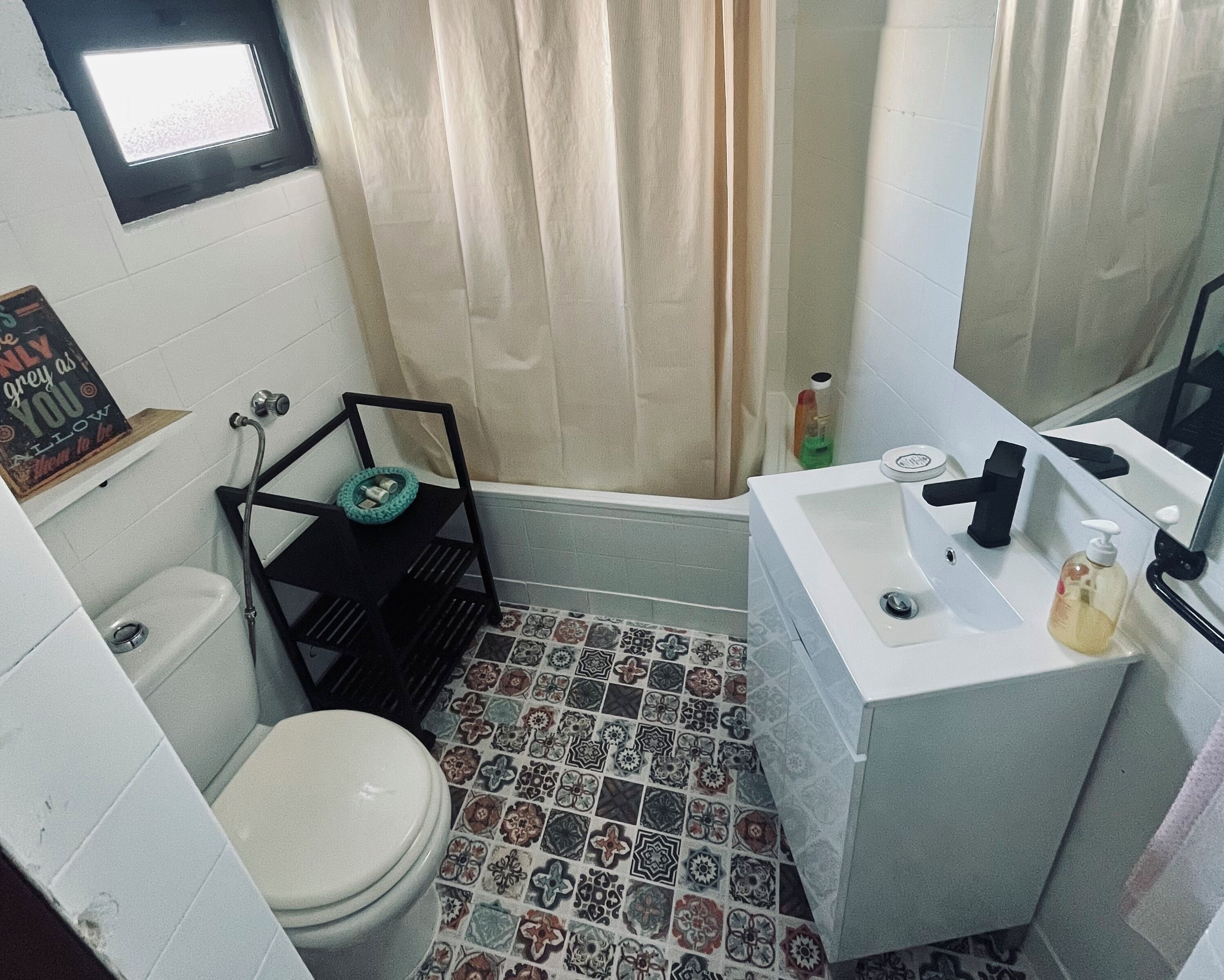 Un baño con inodoro, lavabo, ducha y suelo de baldosas.