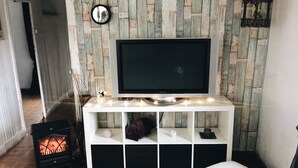 A living room with a flat-screen TV on a white console, a small fireplace, and a clock on the wall.