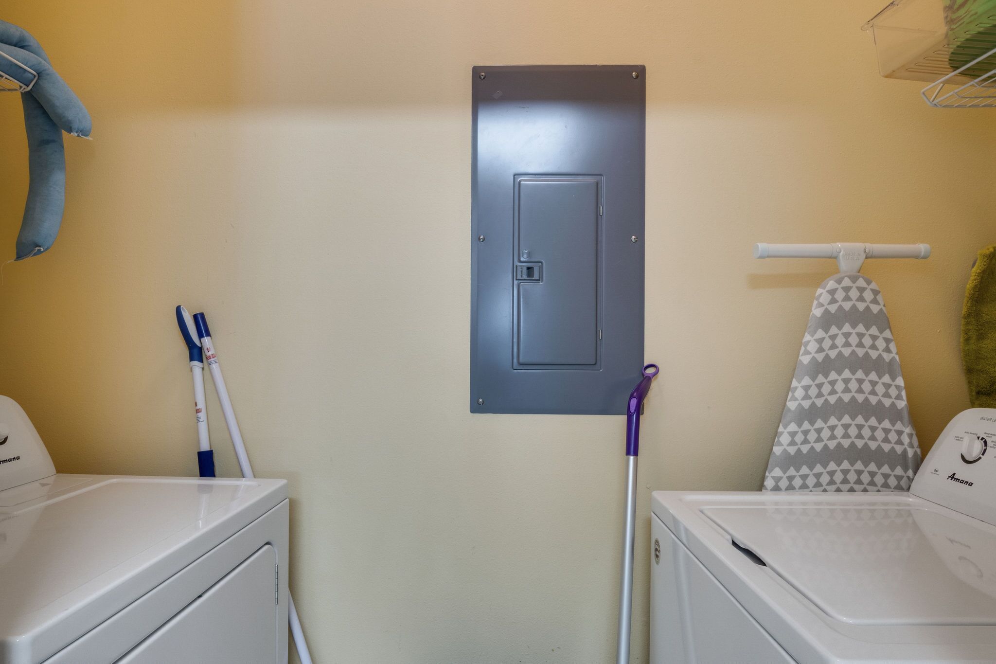 Un área de lavandería con dos lavadoras, un tendedero y un tablero eléctrico en la pared.