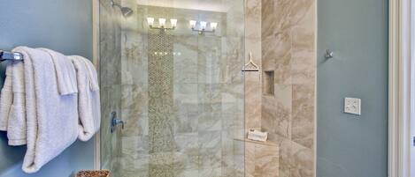 A glass-enclosed shower with a tiled floor, a towel rack, and a small shelf with a folded towel.