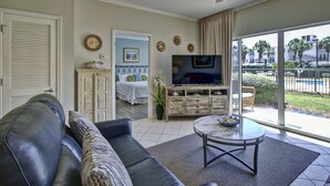 A living room with a leather sofa, a TV on a wooden cabinet, and a view of a pool outside. - Great Location- Heart of Miramar Beach! So Close to Pool, Beach, & More! (Miramar Beach)