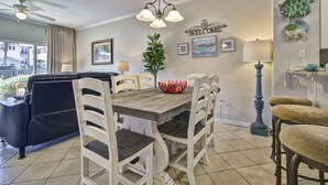 A dining area with a wooden table and white chairs, a blue sofa, and a ceiling fan. - Great Location- Heart of Miramar Beach! So Close to Pool, Beach, & More! (Miramar Beach)