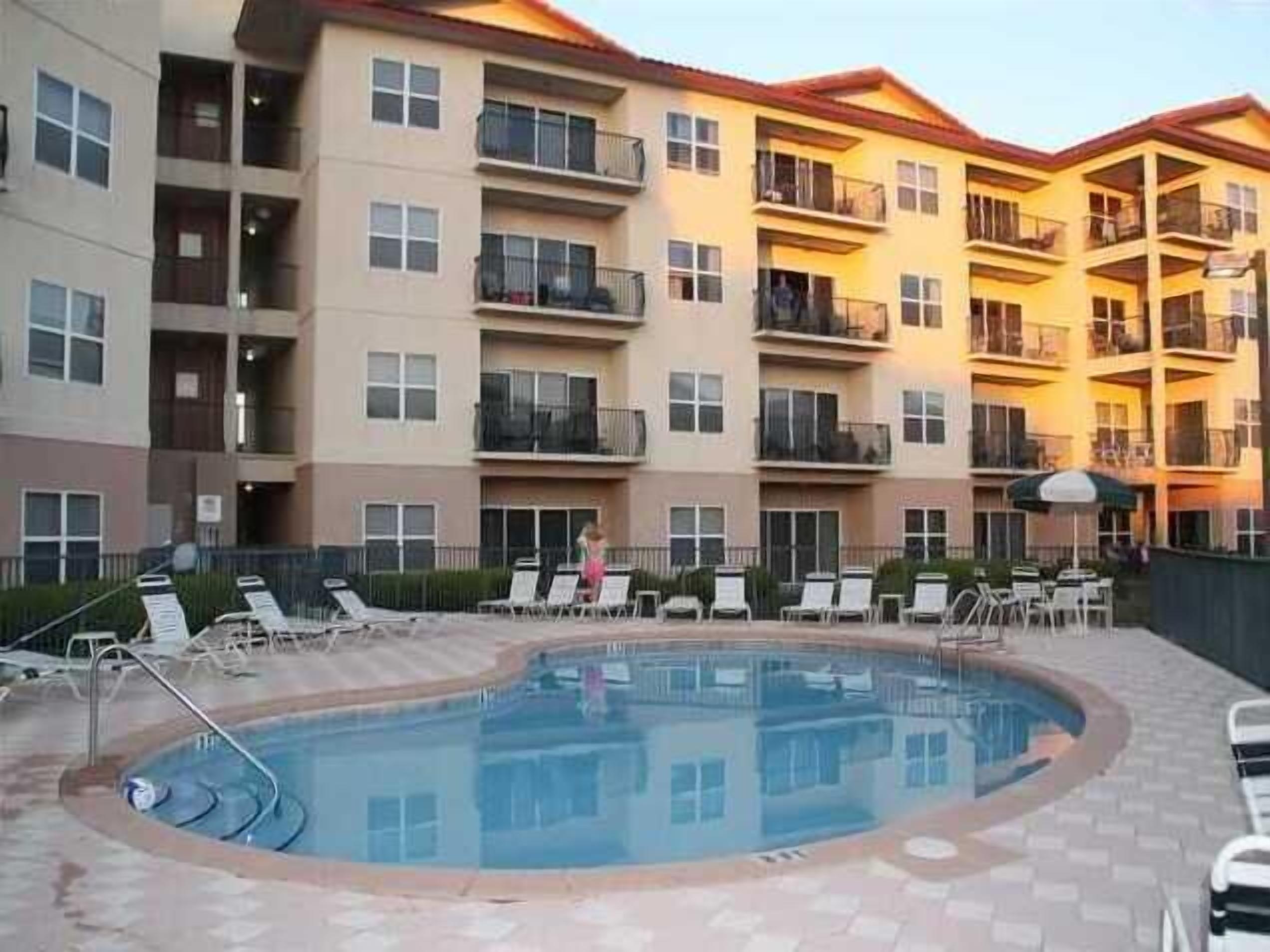 A multi-story residential building with balconies, a swimming pool, and outdoor seating.