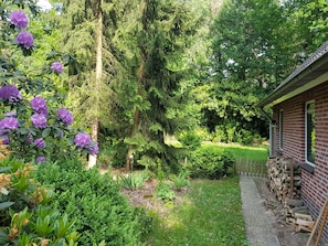 En trädgård med en byggnad av tegel, tät grönska och lila blommor.