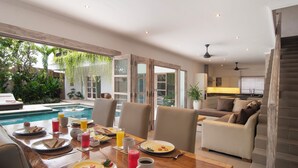 A dining area with a pool view, a sofa, and a staircase. - Puri Temple; fully serviced 3 Bedroom Villa, central Canggu, close to the beach. (Canggu)